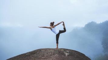 mujer joven ejercita yoga en las montañas. naturaleza de viaje de mujer asiática. viajes relajarse ejercicios yoga touch niebla natural en el pico de la montaña. foto