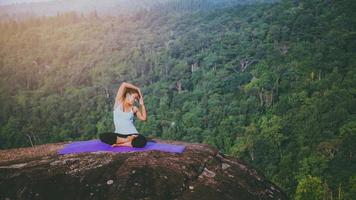 las mujeres asiáticas se relajan en las vacaciones. jugar si yoga. en el acantilado de roca de montaña. naturaleza de los bosques de montaña en tailandia