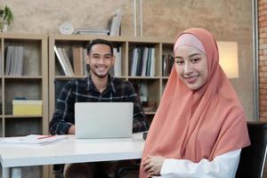 Retrato de empresario de inicio de negocios, joven y bella propietaria, dos socios islámicos, mirando a cámara, sonríe felizmente en la pequeña oficina de trabajo de comercio electrónico.