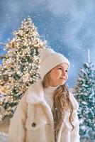 Linda chica rubia caucásica en abrigo de piel ecológica blanca, sombrero y guantes caminando en el bosque de Navidad de invierno. año nuevo, cuento de hadas, concepto de moda. foto