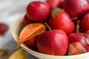 Hermosas manzanas rojas frescas con hojas de otoño en un jarrón de madera foto