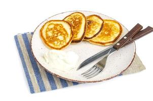 Fried pancakes with sour cream, fork and knife on plate, colored napkin photo