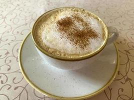 Hot delicious cappuccino with foam and cinnamon in vintage cup on table photo