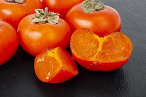 Sweet juicy orange persimmon on contrasting black background. Studio Photo