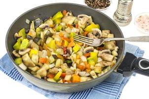 Frying pan with fried seasonal vegetables and mushrooms on white photo