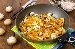 sartén con champiñones champiñones fritos, cebollas y zanahorias sobre fondo de madera. foto de estudio