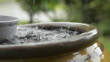 cerrar la lluvia que cae en una vasija de barro con un cuenco de agua flotante en la parte superior. video
