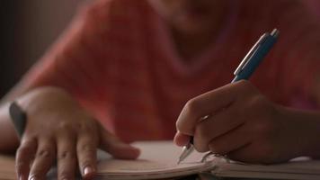 close-up van de hand van een tienermeisje dat op een boek schrijft terwijl ze haar huiswerk doet. video