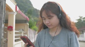 adolescente asiático usando fones de ouvido e um smartphone video