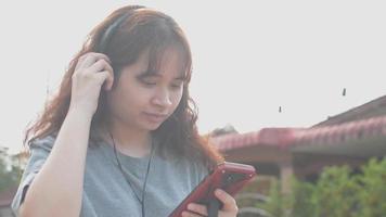 Adolescente asiático usando audífonos y usando un teléfono inteligente video
