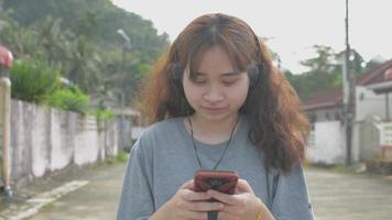 mujer joven asiática escuchando música desde el teléfono inteligente y caminando tranquilamente por la calle.