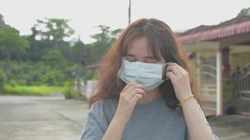 Asian female teenager wearing face mask standing outside of her house.