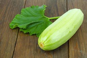 Fresh white zucchini zucchini with green leaf lies on wooden surface. Studio Photo