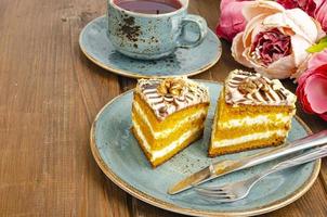 Two pieces of carrot cake on blue plate, cup of tea on wooden table photo