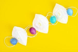 Concept of quarantine at Easter. Decorative eggs and white protective masks on bright background. Social distancing photo