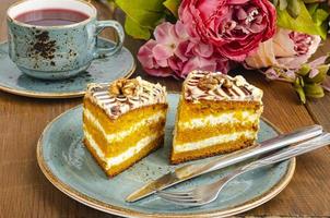 Dos trozos de tarta de zanahoria en la placa azul, una taza de té en la mesa de madera foto