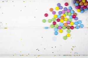 Colored candy bonbons scattered on white wooden board background photo