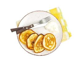 Fried pancakes with sour cream, fork and knife on plate, colored napkin photo