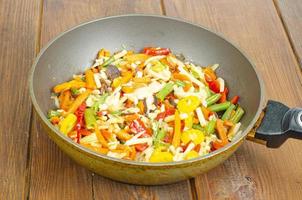 Bright mix of stewed vegetables in frying pan on wooden background photo