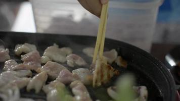 Nahaufnahme von rohem Schweine- und Tintenfischfleisch, das in der heißen Pfanne gegrillt wird.