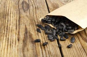 Black unpeeled sunflower seeds in craft bag on wooden table.