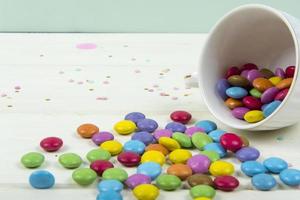 Colored candy bonbons scattered on white wooden board background photo