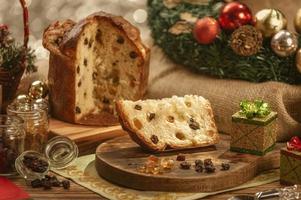 A slice of panettone and candied fruit cubes on wooden cutting board with christmas ornaments photo