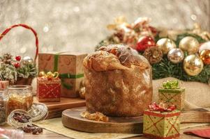 Panettone, pasas y cubos de fruta confitada sobre tabla de cortar de madera con adornos navideños foto