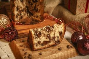 Slice of chocolate panettone  on wooden cutting board with christmas ornaments photo