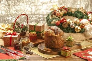 Panettone, pasas y cubos de fruta confitada sobre tabla de cortar de madera con adornos navideños foto