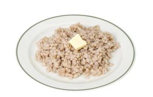 Gachas de avena, cebada perlada hervida en un plato sobre fondo blanco.