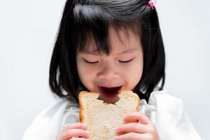 Portrait little girl eating white bread. On white background. photo