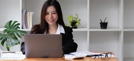 Mujer asiática de negocios con ordenador portátil para hacer finanzas matemáticas en un escritorio de madera en la oficina, impuestos, contabilidad, concepto financiero