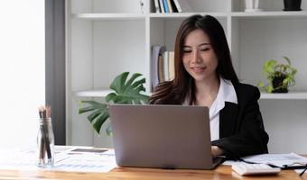 Mujer asiática de negocios con ordenador portátil para hacer finanzas matemáticas en un escritorio de madera en la oficina, impuestos, contabilidad, concepto financiero foto