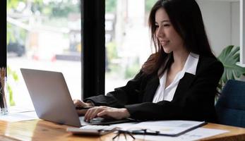 Mujer asiática de negocios con ordenador portátil para hacer finanzas matemáticas en un escritorio de madera en la oficina, impuestos, contabilidad, concepto financiero