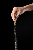 Hand sprinkling ground pepper isolated on black background photo