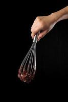 Chef holding wire whisk and melted chocolate on black background photo