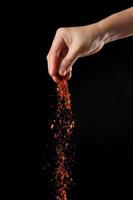 Hand sprinkling cayenne pepper on black background photo