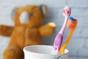 colorful child toothbrushes in white mug against a wall photo