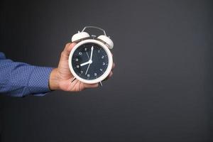 person hand holding alarm clock against gray background , photo