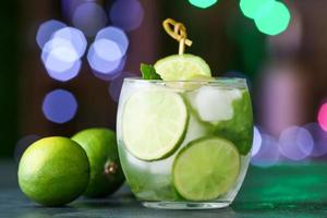 Glass of cold mojito on table against blurred lights photo