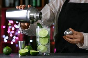 Female bartender making fresh mojito on table in bar photo