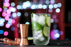 Glass of cold mojito on table against blurred lights photo