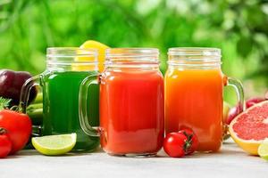 Frascos de albañil con jugos saludables, frutas y verduras en la mesa al aire libre, primer plano