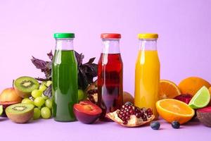 Botellas con jugos saludables y frutas sobre fondo de color foto