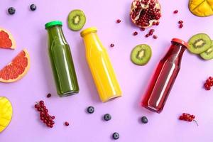 Bottles with healthy juice and fruits on color background photo