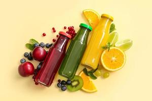 Bottles with healthy juice and fruits on color background photo