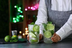 Camarero femenino con vasos de mojito fresco en la mesa en el bar foto