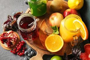 Frascos de albañil con jugos saludables, frutas y verduras sobre fondo oscuro