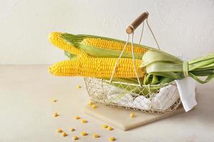 Basket with fresh corn cobs on light background photo